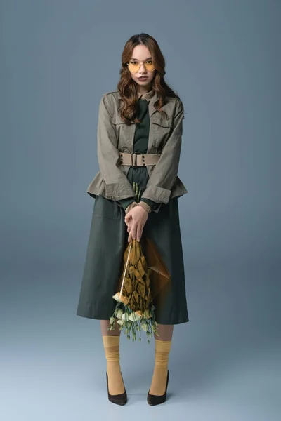 Stylish girl posing in autumn outfit with bouquet of flowers, isolated on grey — Stock Photo