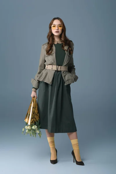 Jolie fille posant en tenue à la mode avec bouquet de fleurs, isolé sur gris — Photo de stock