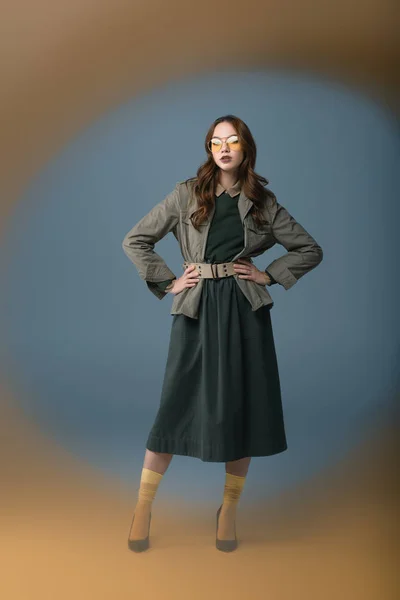 Beautiful model posing in autumn outfit and yellow sunglasses, isolated on grey with orange filter — Stock Photo