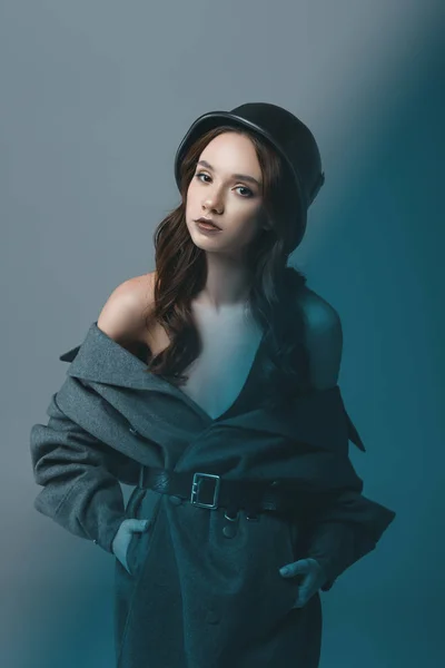 Sensual model posing in autumn coat and military helmet, isolated on grey with blue filter — Stock Photo