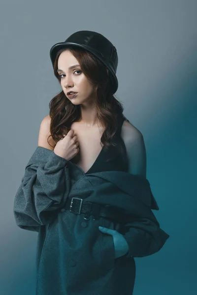 Attractive girl posing in autumn coat and military helmet, isolated on grey with blue filter — Stock Photo