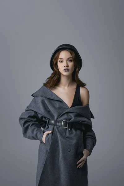 Chica elegante posando en abrigo de otoño y casco militar, aislado en gris - foto de stock