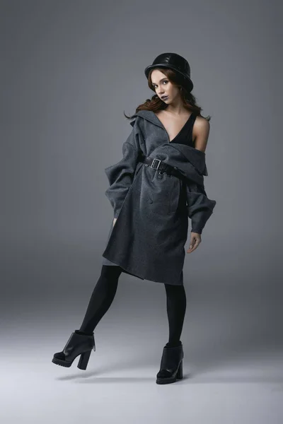 Seductive fashionable girl posing in autumn coat and military helmet, isolated on grey — Stock Photo