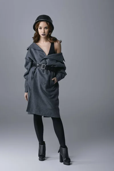 Fashionable girl posing in autumn coat and military helmet, isolated on grey — Stock Photo