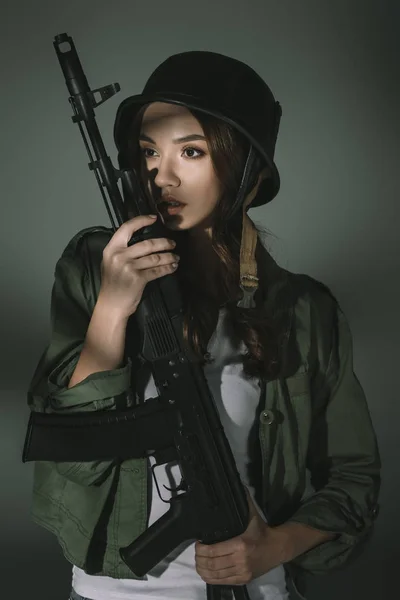 Jolie jeune fille en casque militaire avec fusil, sur gris avec des ombres — Photo de stock