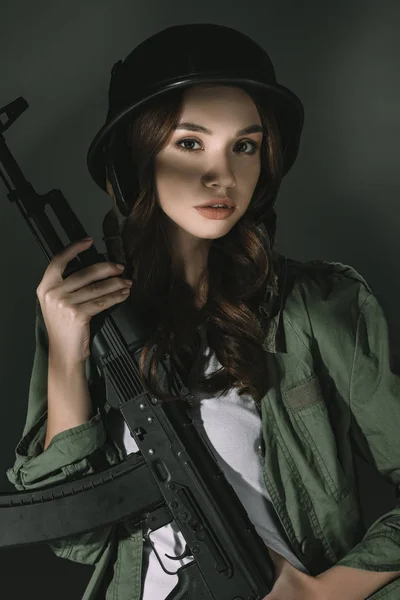 Bella ragazza caucasica in casco militare con fucile, su grigio con ombre — Foto stock