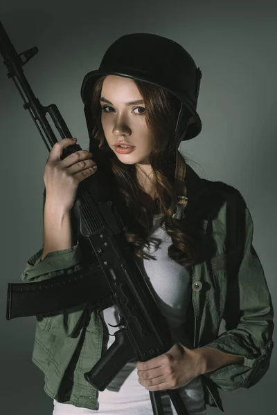 Attraente ragazza in casco militare con fucile, su grigio con ombre — Foto stock