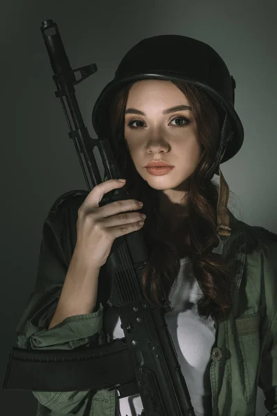 Belle jeune femme au casque militaire avec fusil, sur gris avec ombres — Photo de stock