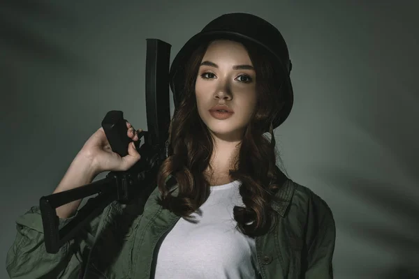 Jolie fille en casque militaire avec fusil, sur gris avec des ombres — Photo de stock