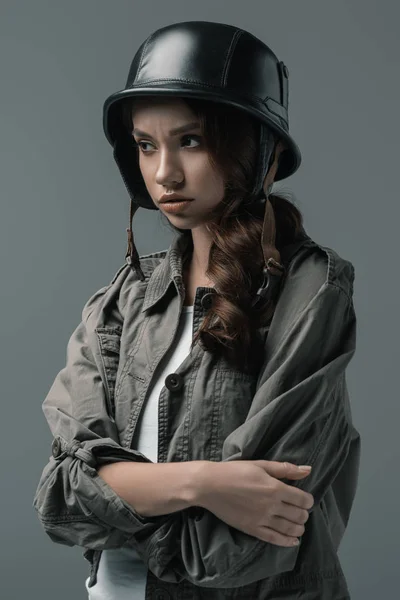 Beautiful worried girl posing in military helmet with crossed arms, isolated on grey — Stock Photo
