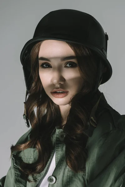 Beautiful girl posing in military helmet with shadows on face, isolated on grey — Stock Photo