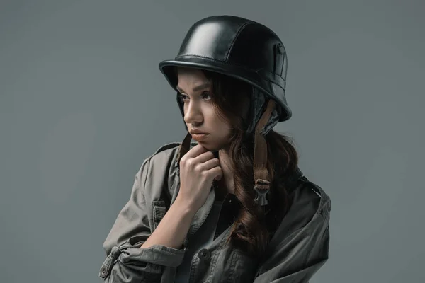 Красивая расстроенная девушка, позирующая в военном шлеме, изолированная на сером — стоковое фото