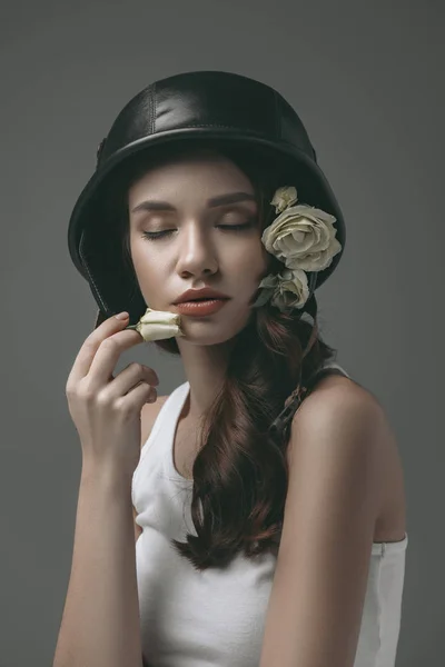 Нежная молодая девушка с закрытыми глазами в военном шлеме с белыми цветами, изолированными на сером — стоковое фото