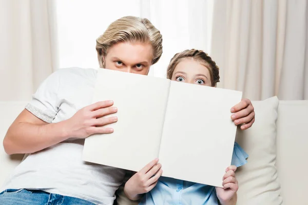 Father and daughter covering face with book — Free Stock Photo