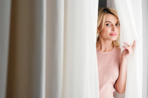 Woman looking out of curtain — Stock Photo, Image