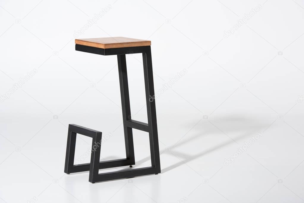 Studio shot of stylish barstool with wooden top and black metallic legs standing on white