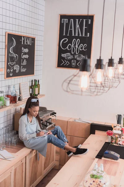 Barista sitting on counter with notebook — Free Stock Photo