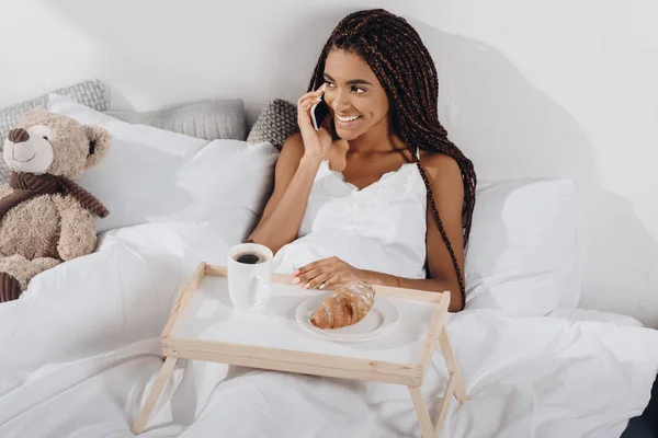 Woman with breakfast in bed and talking by phone — Stock Photo, Image