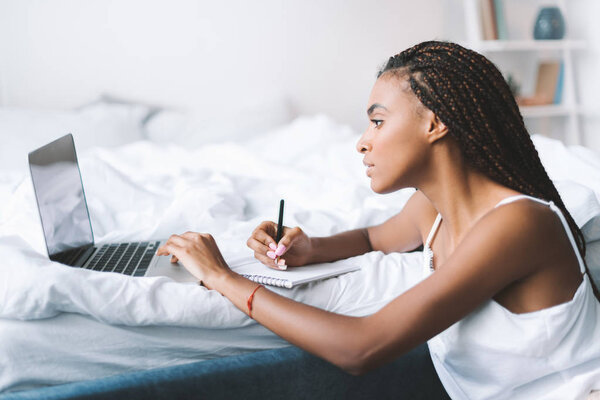 woman with laptop in bed writing in notepad