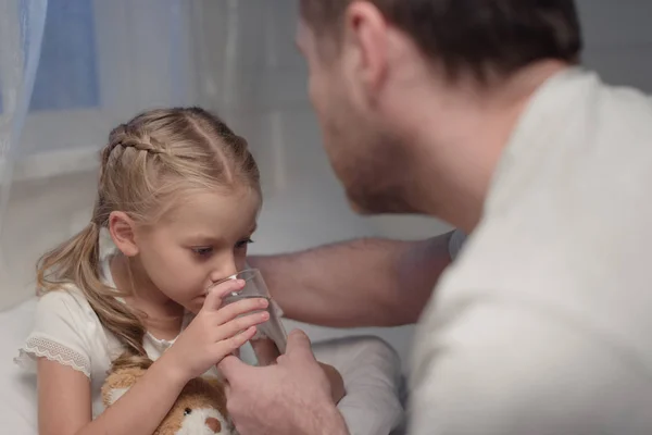 Father giving water to daughter in bed — Stock Photo, Image