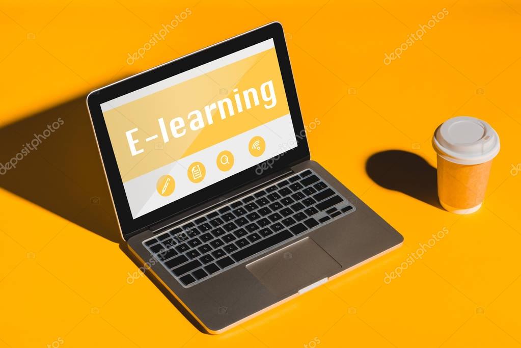 Laptop with e-learning inscription on screen and coffee to go on orange