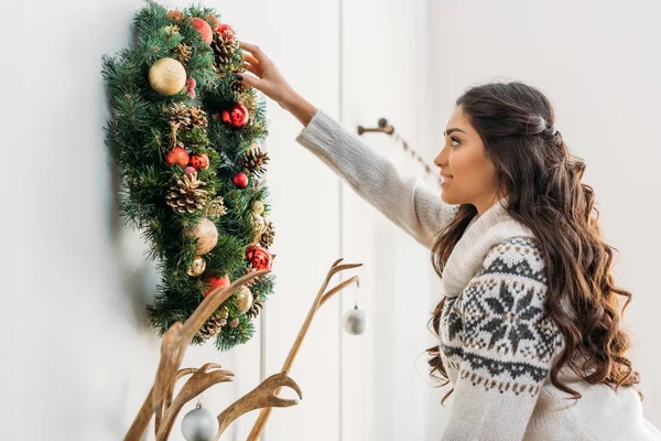 Woman hanging christmas wreath over fireplace — Stock Photo, Image