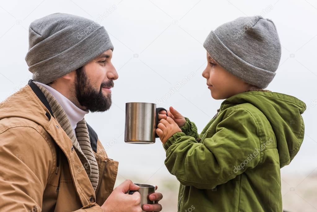 father and son with hot drinks outdoors