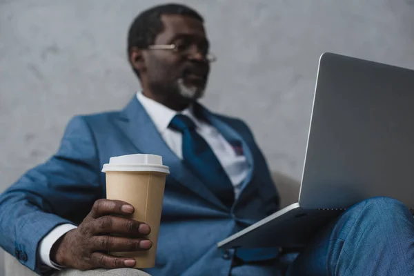 Mann sitzt im Sessel mit Laptop und Kaffee — Stockfoto