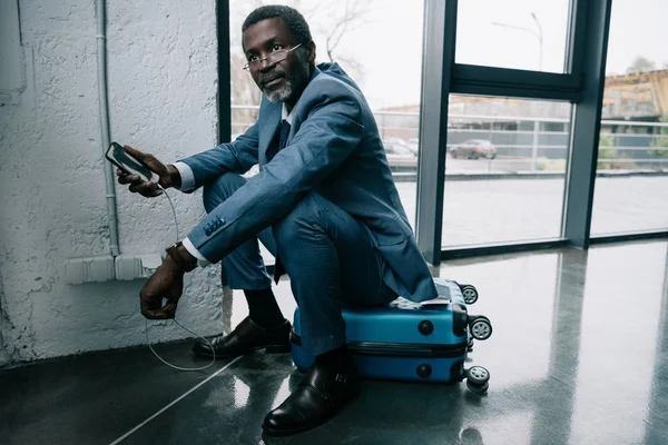 Hombre de negocios esperando carga de teléfonos inteligentes en el aeropuerto —  Fotos de Stock