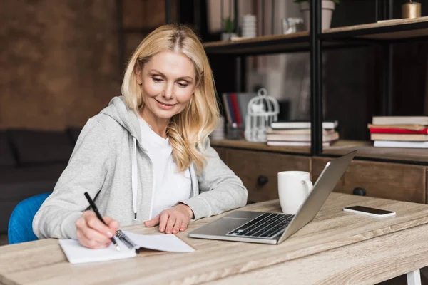 Woman taking notes and using laptop — Stock Photo, Image