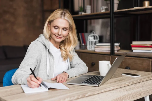 Mujer tomando notas y utilizando el ordenador portátil —  Fotos de Stock