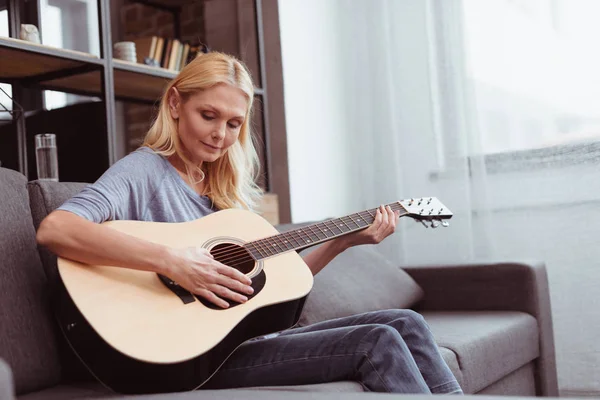 Женщина среднего возраста с гитарой дома — стоковое фото