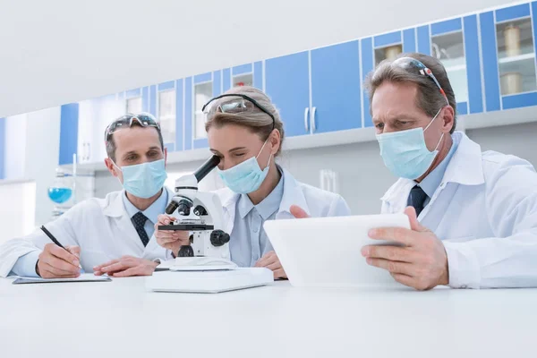 Científicos trabajando con microscopio y tableta — Foto de Stock