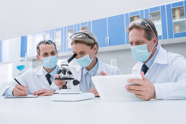 Scientists working with microscope and tablet