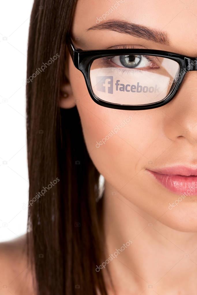 Portrait of young woman with facebook logo reflection in eyeglasses isolated on white