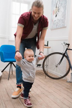smiling father teaching baby boy to walk at home clipart