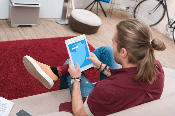 man sitting on sofa while using digital tablet with twitter appliance