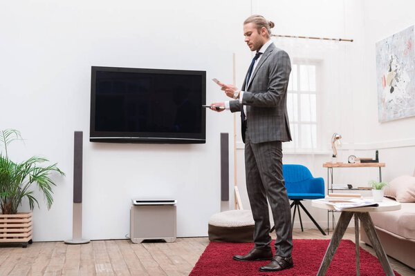 Бизнесмен смотрит на смартфон и держит пульт дистанционного управления
