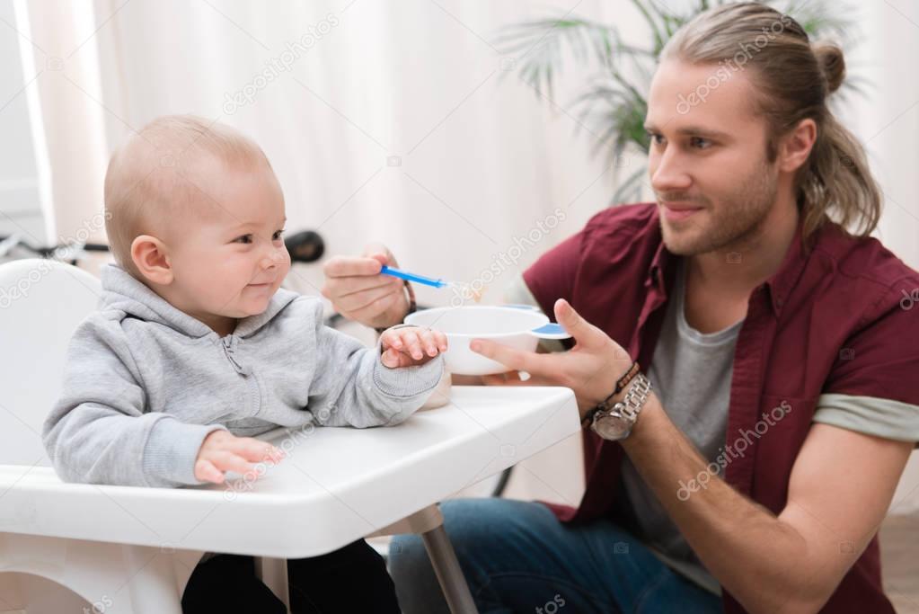 father feeding his cheerful son with baby food at home