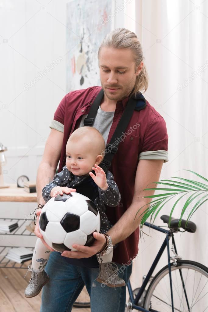 father with son in baby sling holding a football ball