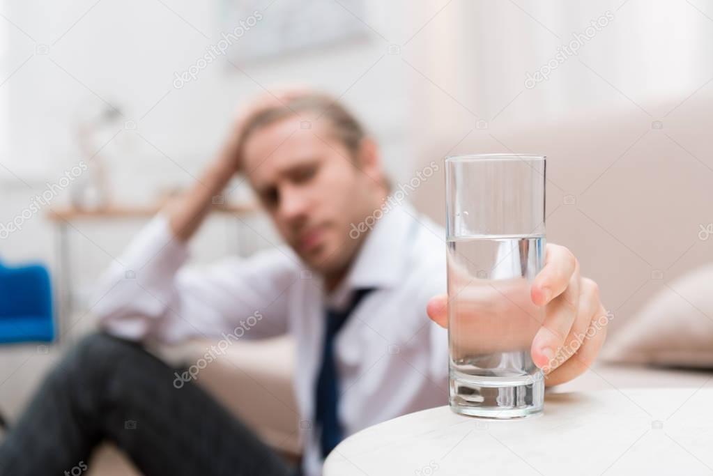 Businessman sitting on a floor at home and taking glass of water