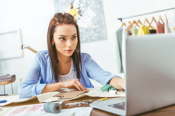 Σοβαρή Μοδίστρα Βλέπουν Laptop Στο Τραπέζι Εργασίας — Φωτογραφία Αρχείου