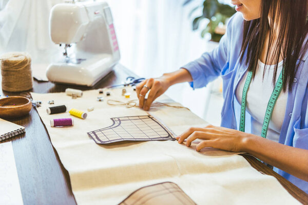 cropped image of smiling seamstress measuring pattern at table 