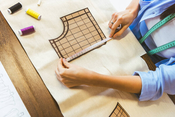 cropped image of seamstress measuring pattern at table 