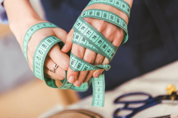 cropped image of seamstress hands winded up with tape measure