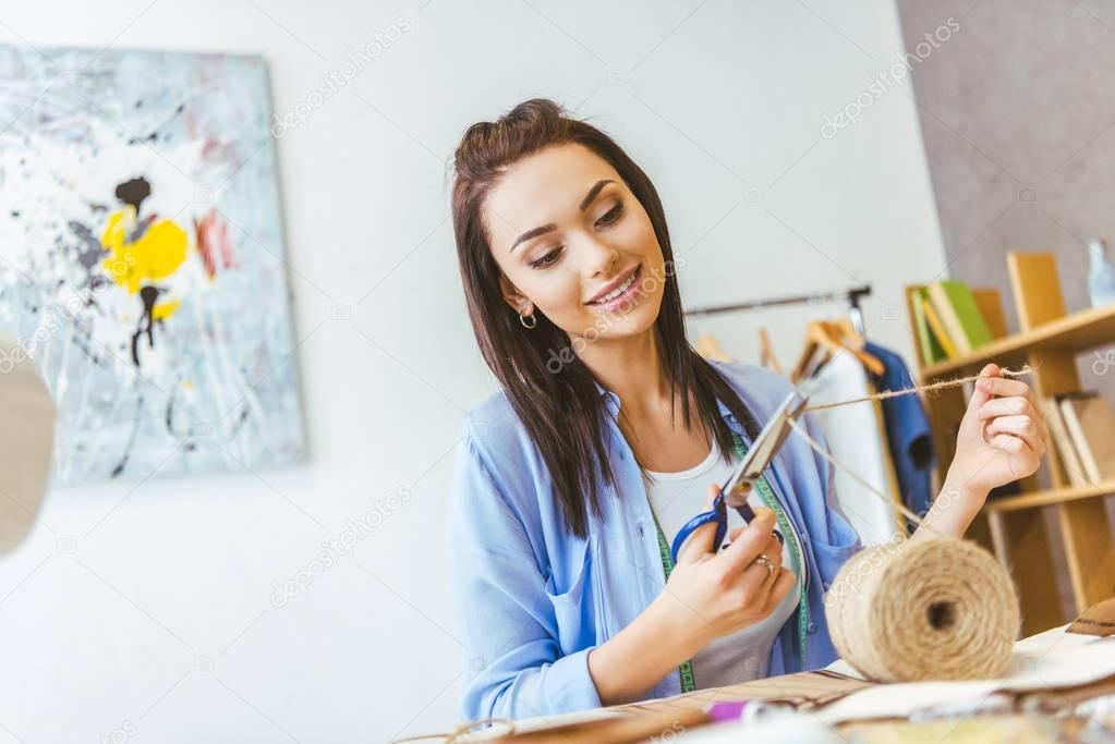 smiling seamstress cutting thread with scissors