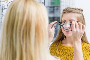 oculist helping client to choose eyeglasses in optics