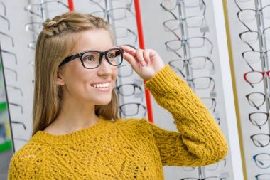 young smiling girl choosing eyeglasses in optics clipart