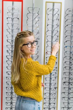 young beautiful girl choosing eyeglasses in optics clipart