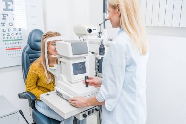 professional female doctor examining patient through slit lamp in clinic clipart